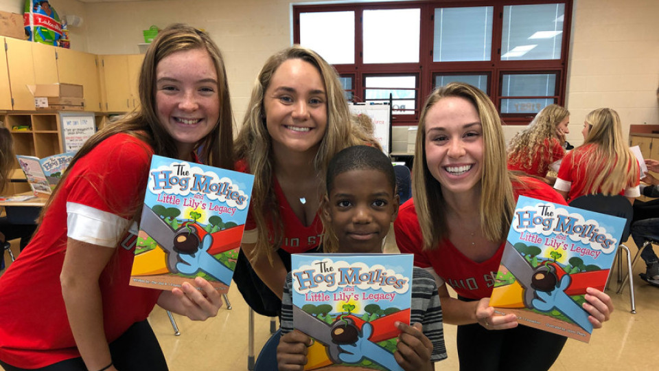 Student athletes standing with child holding hog mollie books